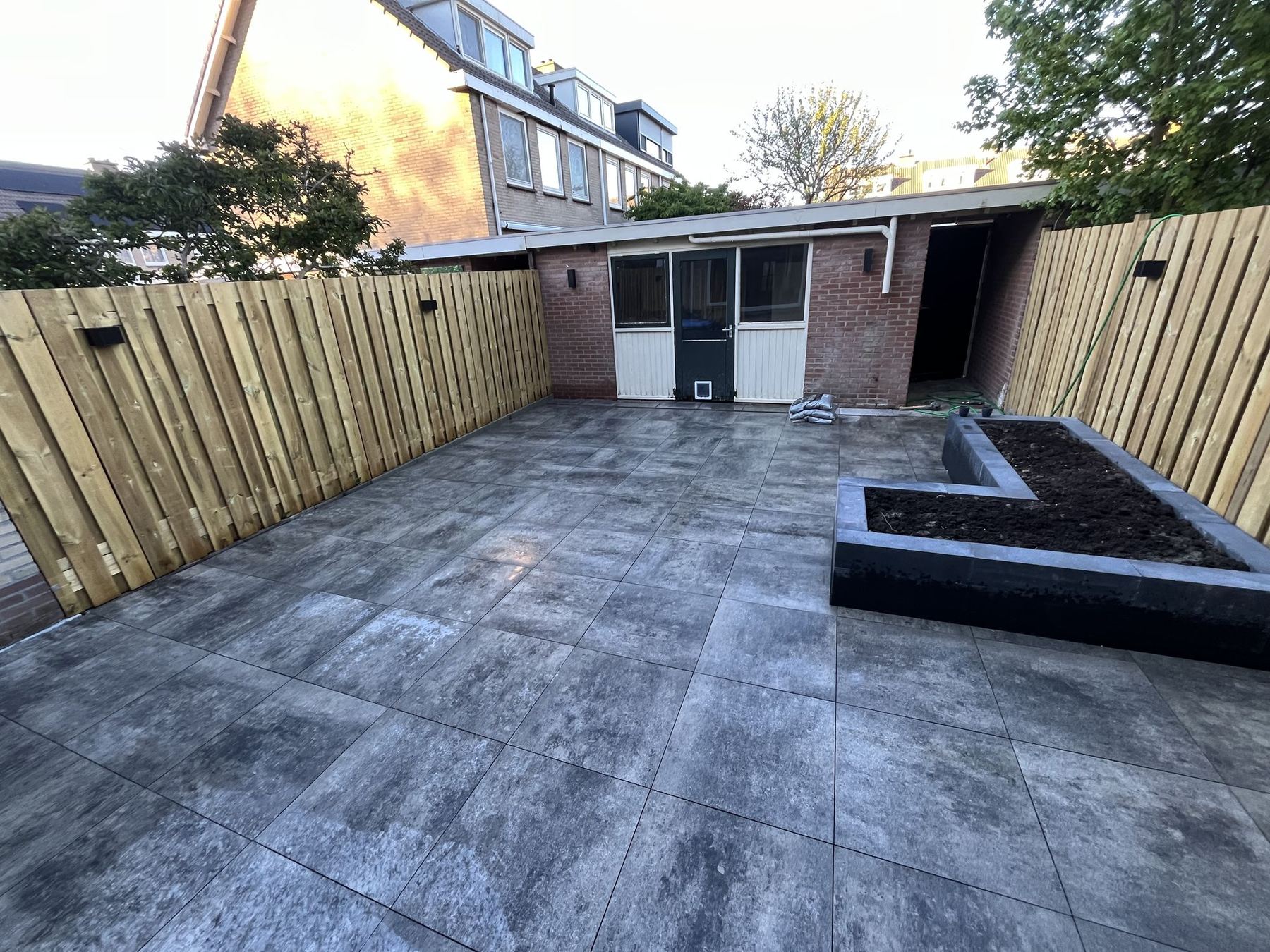 Aangelegde achtertuin met keramische tegels en plantenbak in Maassluis